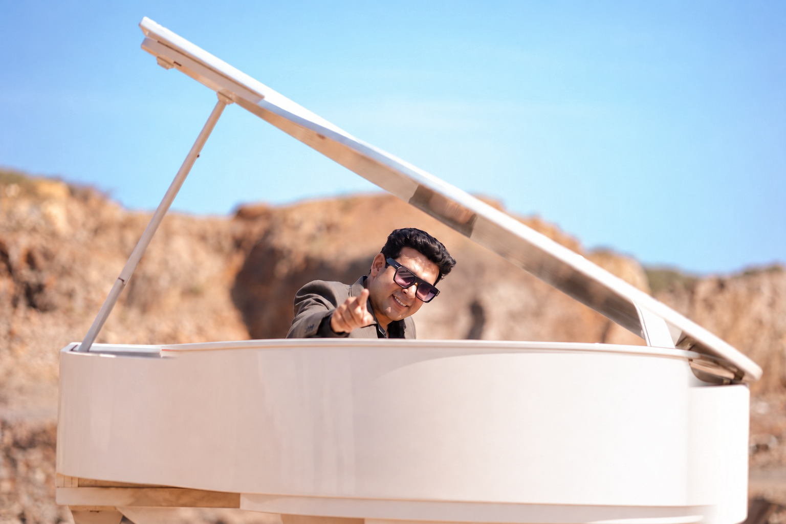 Dr. Aman Bathla at a white piano, pointing toward the viewer